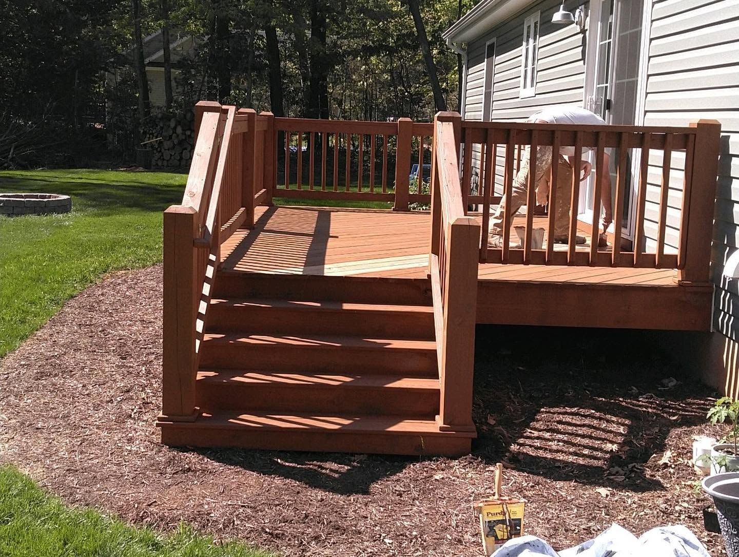 Wooden backyard deck with steps, railing, and lattice skirt beside a house, surrounded by mulch and grass