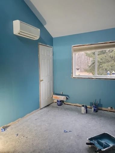 Empty blue room with a wall-mounted air conditioner, window, and paint supplies on the floor