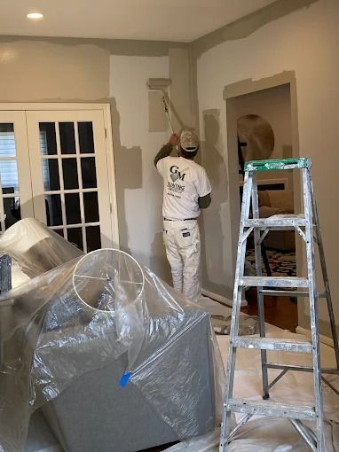 Two people painting a room gray beside a ladder and covered furniture.