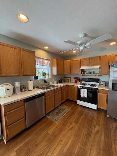 Bright kitchen with wooden cabinets, white appliances, and wood flooring.