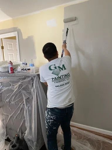 Painter rolling light gray paint on an interior wall in a room under renovation