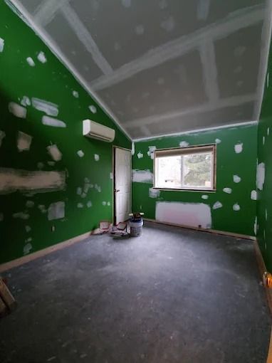 Empty green room under renovation with white drywall patches, gray floor, and a window.