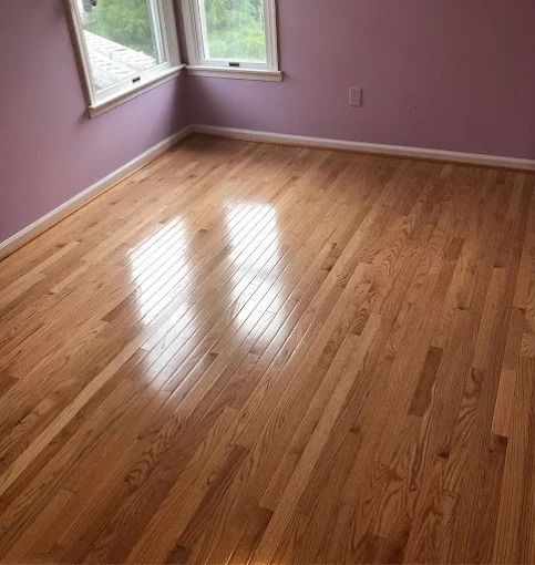 Empty room with glossy hardwood floor, lavender walls, and sunlit windows