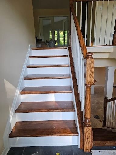 Interior staircase with white risers, dark wood treads, and a wooden banister beside a hallway.