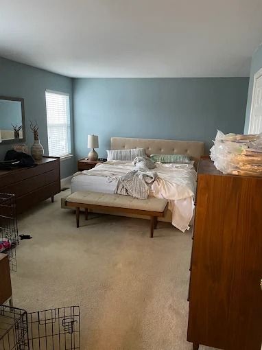 A messy bedroom with an unmade bed, light blue walls, dresser, and wooden wardrobe.