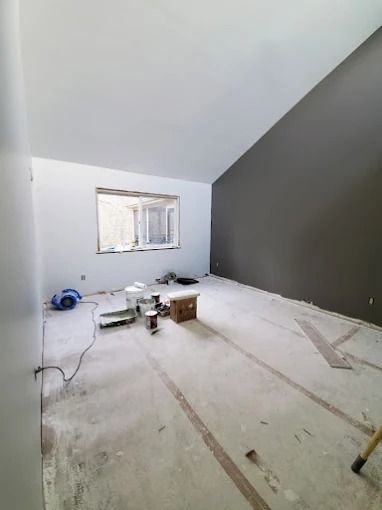 Empty room under renovation with white walls, dark accent wall, window, and tools scattered on the floor