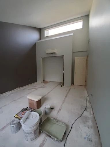 Renovation room with high window, bare walls, floor coverings, paint buckets, and tools on the floor