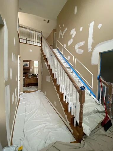 Staircase and hallway under renovation, with plastic floor covering and taped drywall patches.