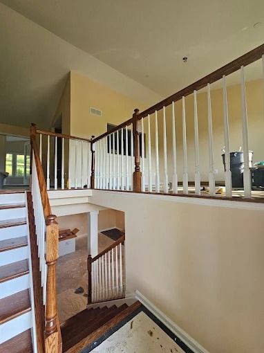 Staircase landing with wooden railing and beige walls overlooking a lower entryway.