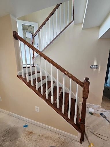 Indoor staircase with wooden banister under construction, surrounded by unfinished flooring and tools