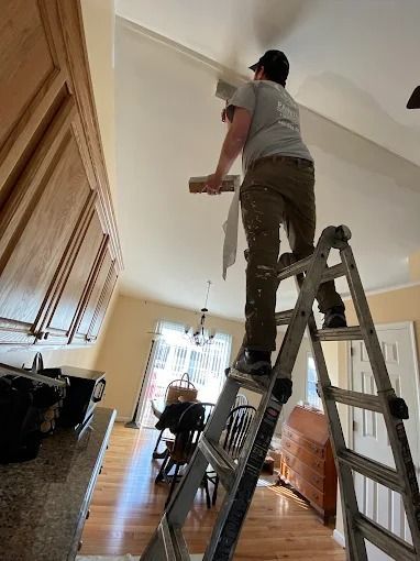 Person on a ladder painting a white ceiling in a home hallway
