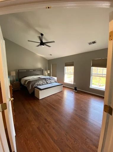 Empty bedroom with hardwood floors, gray walls, ceiling fan, and bed by the left wall.