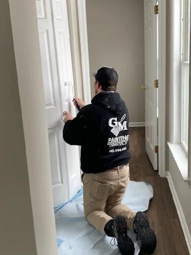 Worker kneeling in a hallway, painting a white door frame during home renovation.