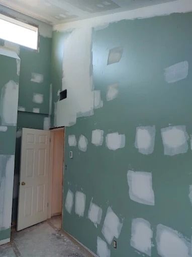 Blue-green room under renovation with drywall patching and an open door under a window.