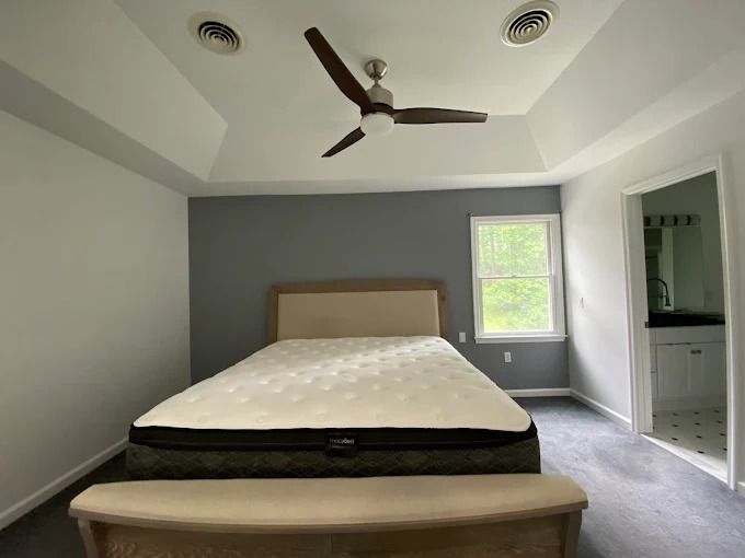 Modern bedroom with a bed, gray accent wall, ceiling fan, and small window.