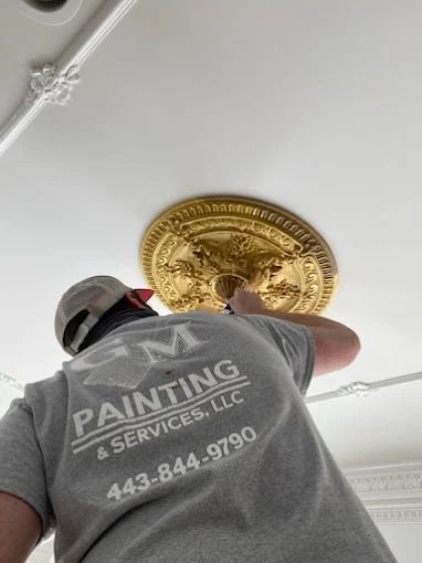 Worker painting a decorative ceiling medallion on a white ceiling
