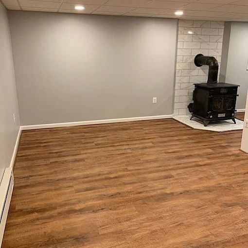 Empty room with gray walls, wood floor, and a black wood stove in the corner.