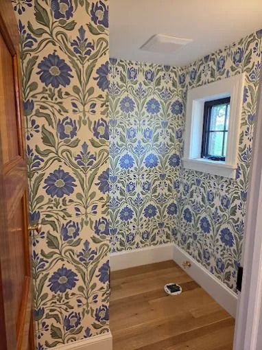 Patterned wallpaper in a small bathroom with a window and wood floor, renovation in progress