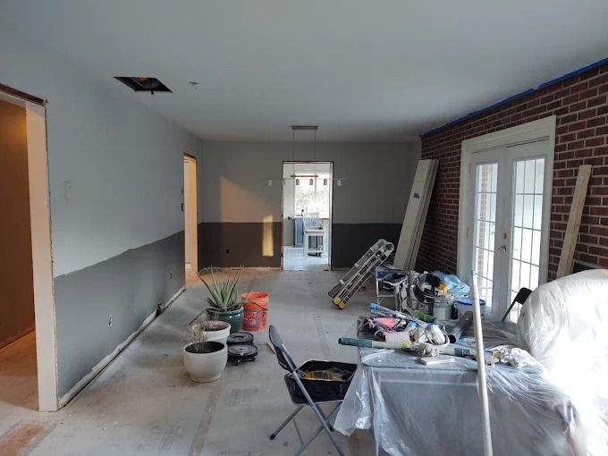 Renovation in progress in a narrow room with tools, paint cans, ladders, and debris along the floor.