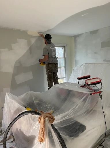 Painter working on patching and painting a room with plastic-covered furniture and supplies