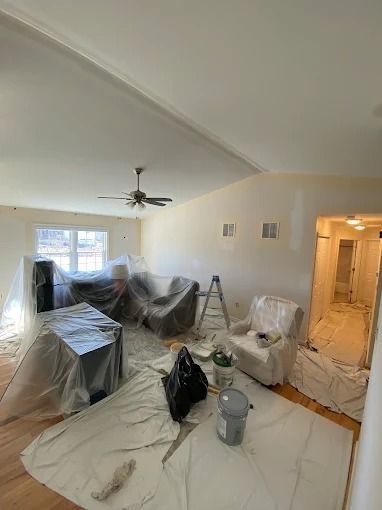 Living room under renovation, furniture covered in plastic and floor protected with drop cloths