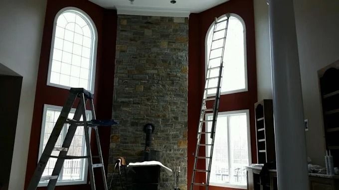 Ladders set up in a room with tall arched windows and a stone fireplace wall.