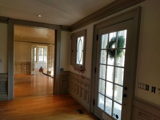 Bright hallway with polished wood floors, paneled walls, and a glass door to a sunlit room.