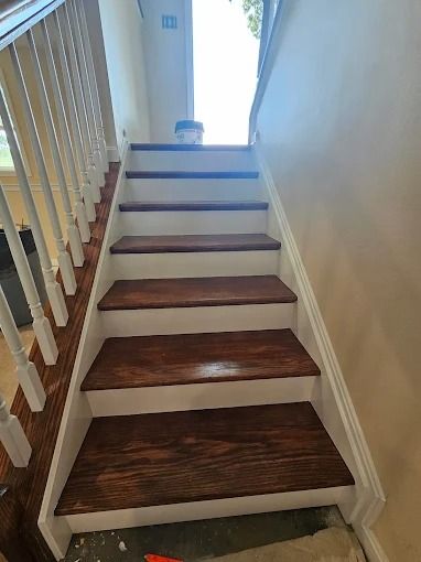 Indoor staircase with white railings, beige walls, and dark wood steps leading up to a bright landing