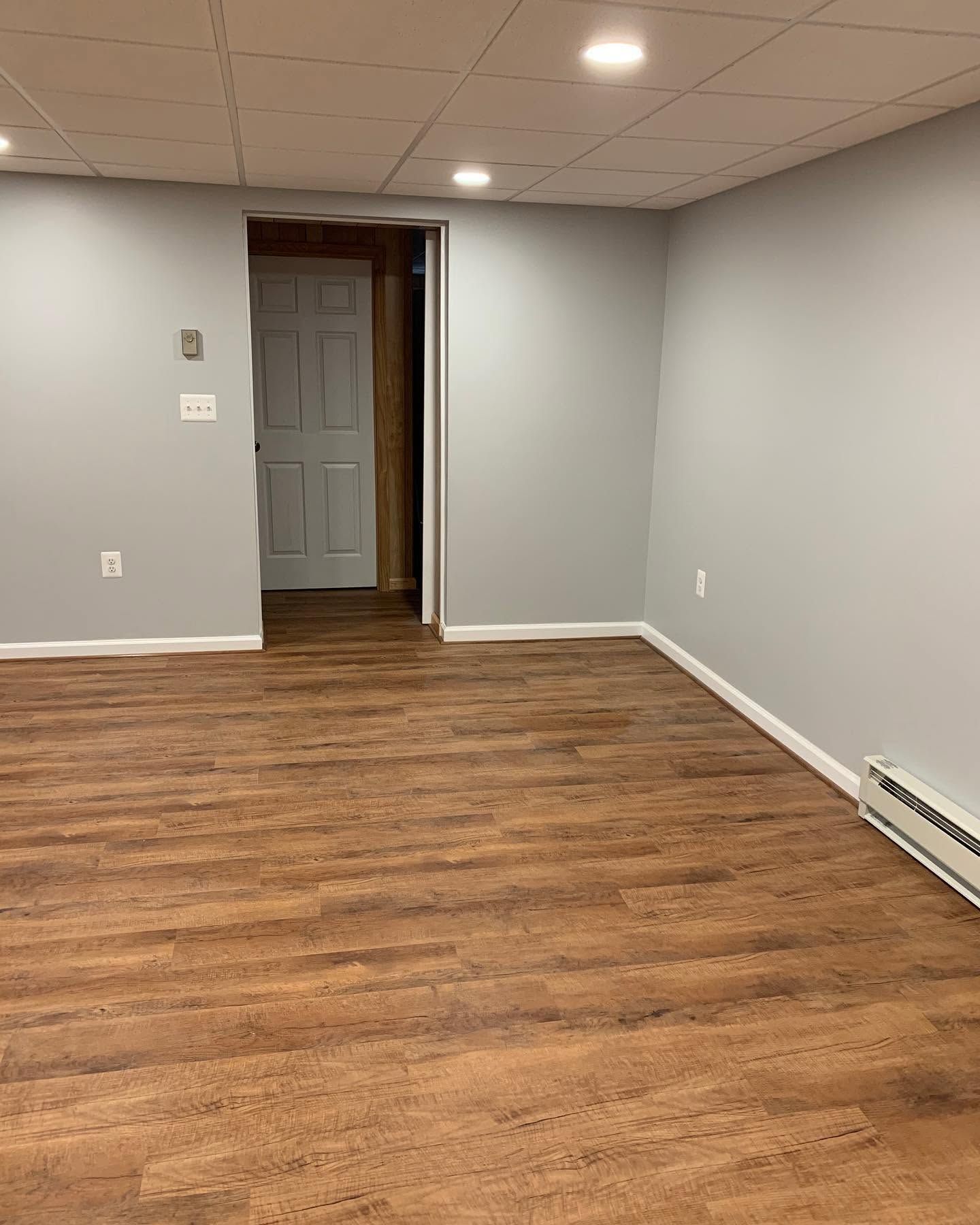 Empty gray room with wood flooring, recessed ceiling lights, and an open doorway.