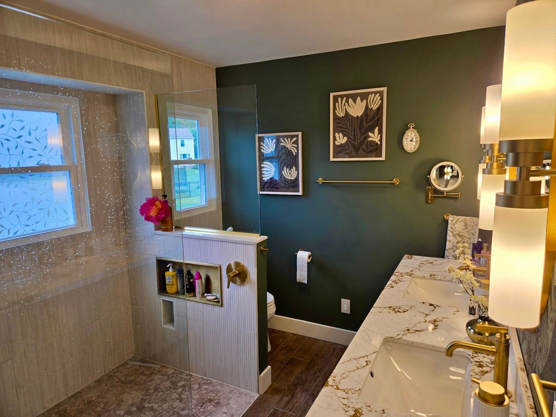 Bathroom with dark green walls, marble vanity, lit sconces, and a window with woven shade.
