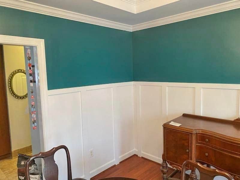 Empty room with teal walls, white wainscoting, and a wooden desk in the corner