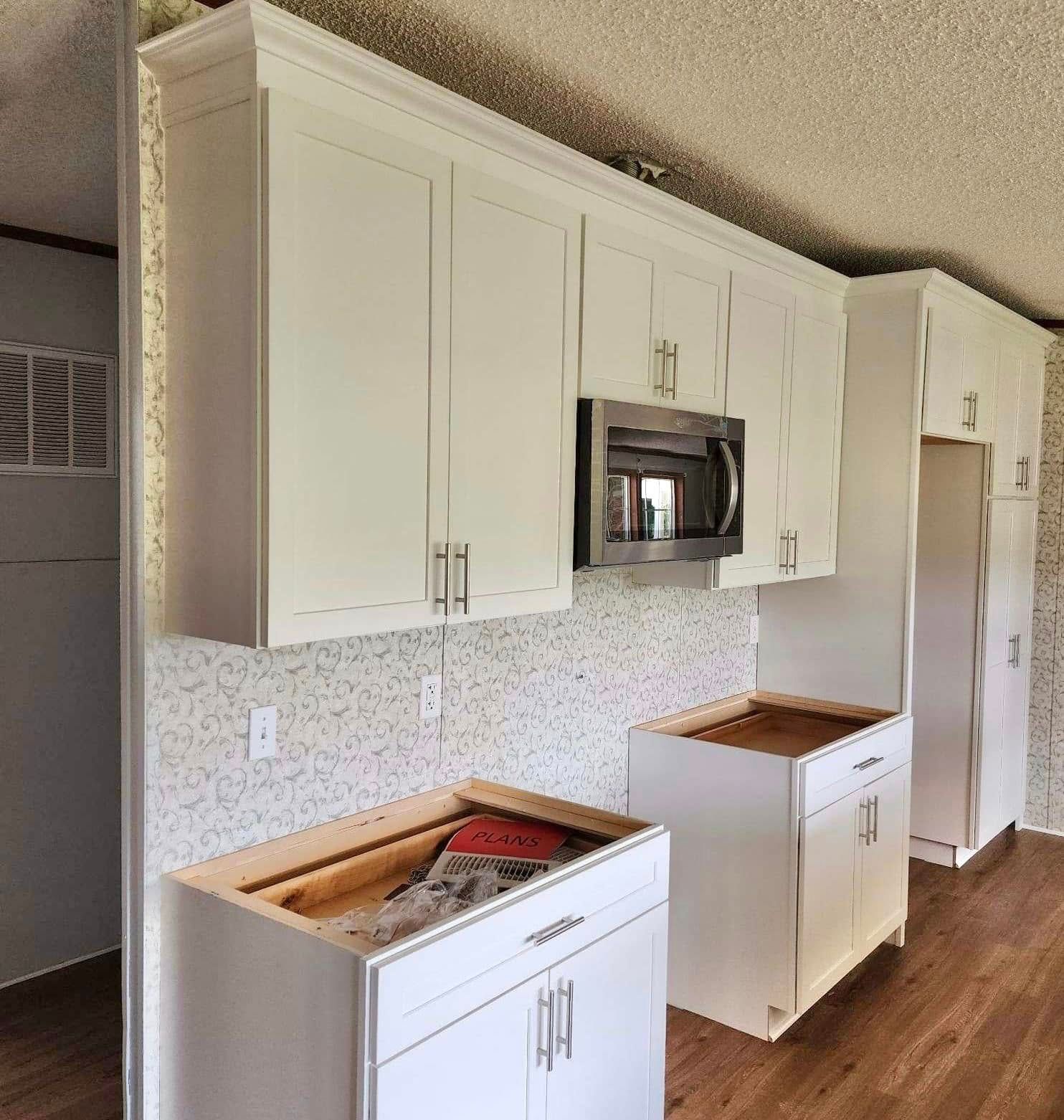 White kitchen cabinets and countertop with brown wood floor in a bright empty room