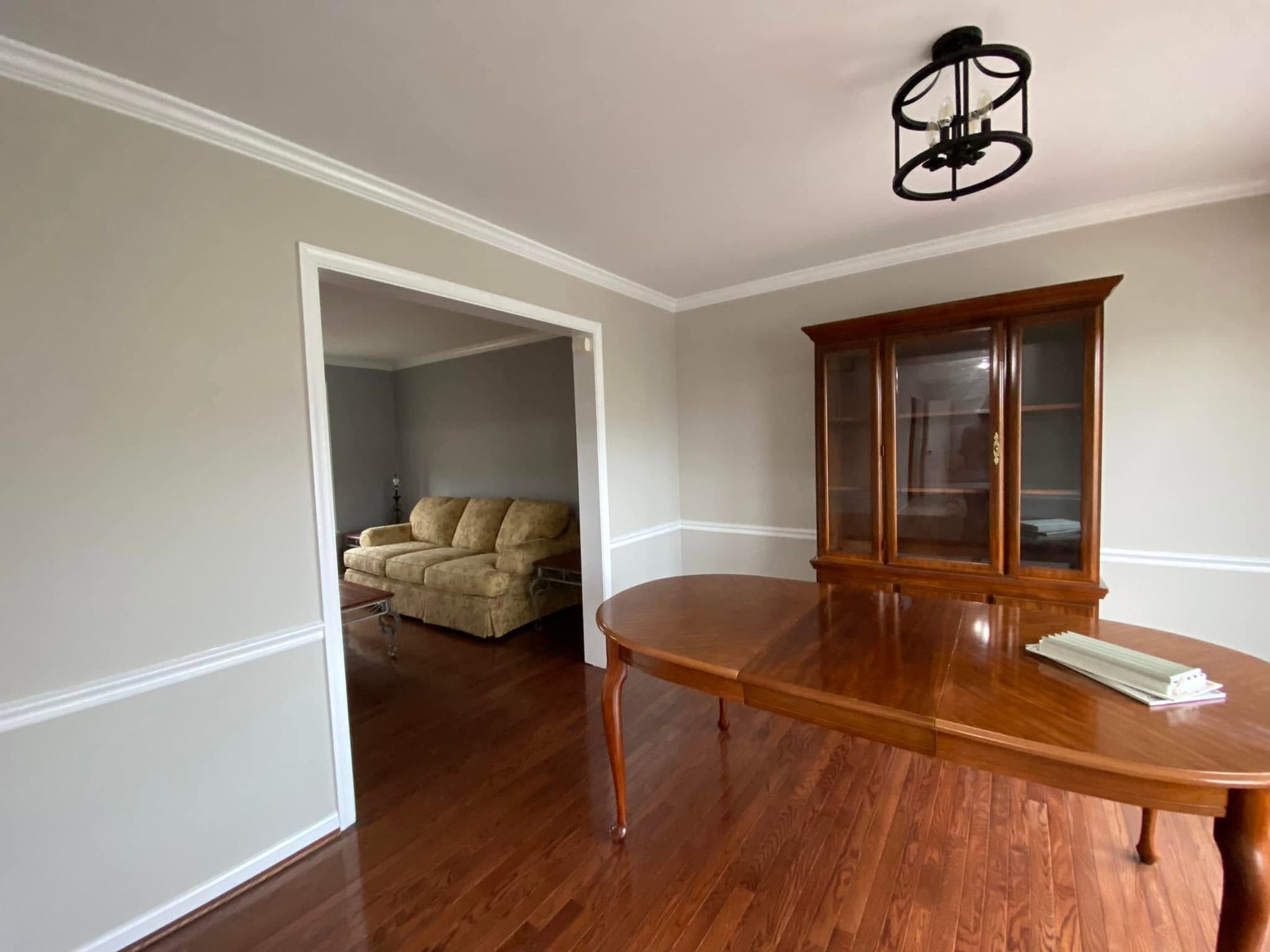Dining room with wooden table and china cabinet, opening into a living room with a beige sofa.