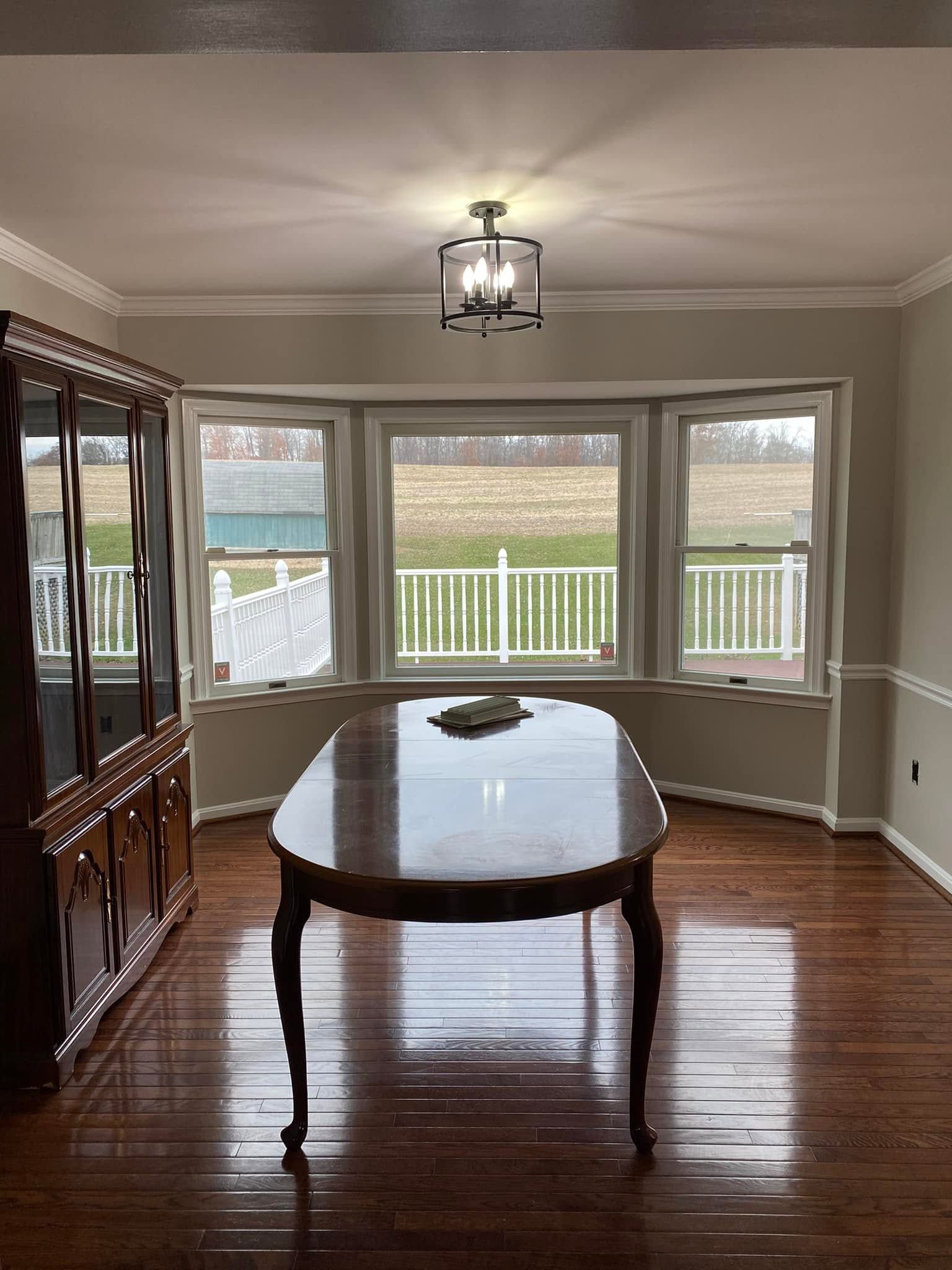 Dining room with polished wood table, china cabinet, and bay windows overlooking a deck and backyard.
