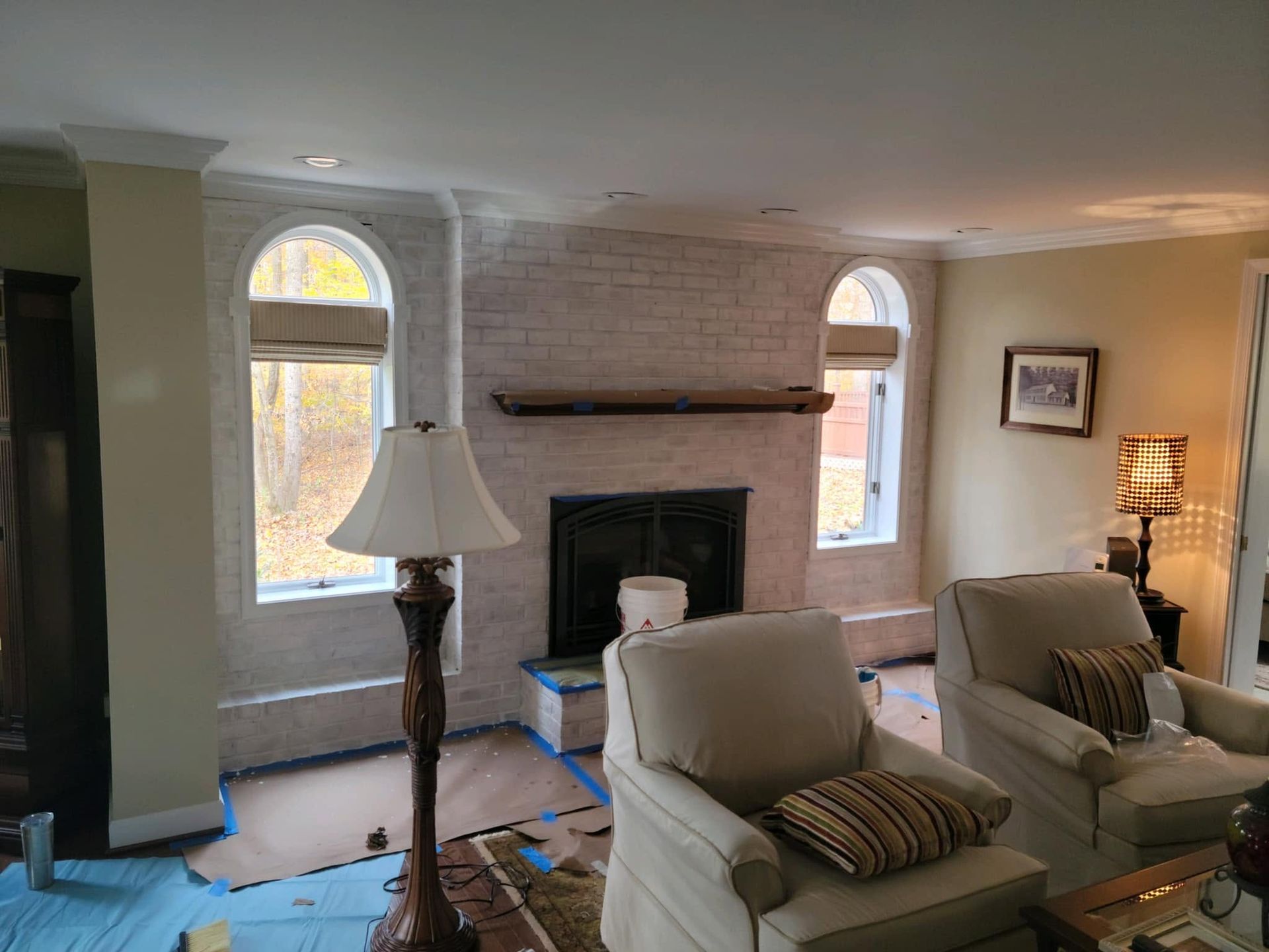 Living room with fireplace, arched windows, white and beige chairs, and a floor lamp