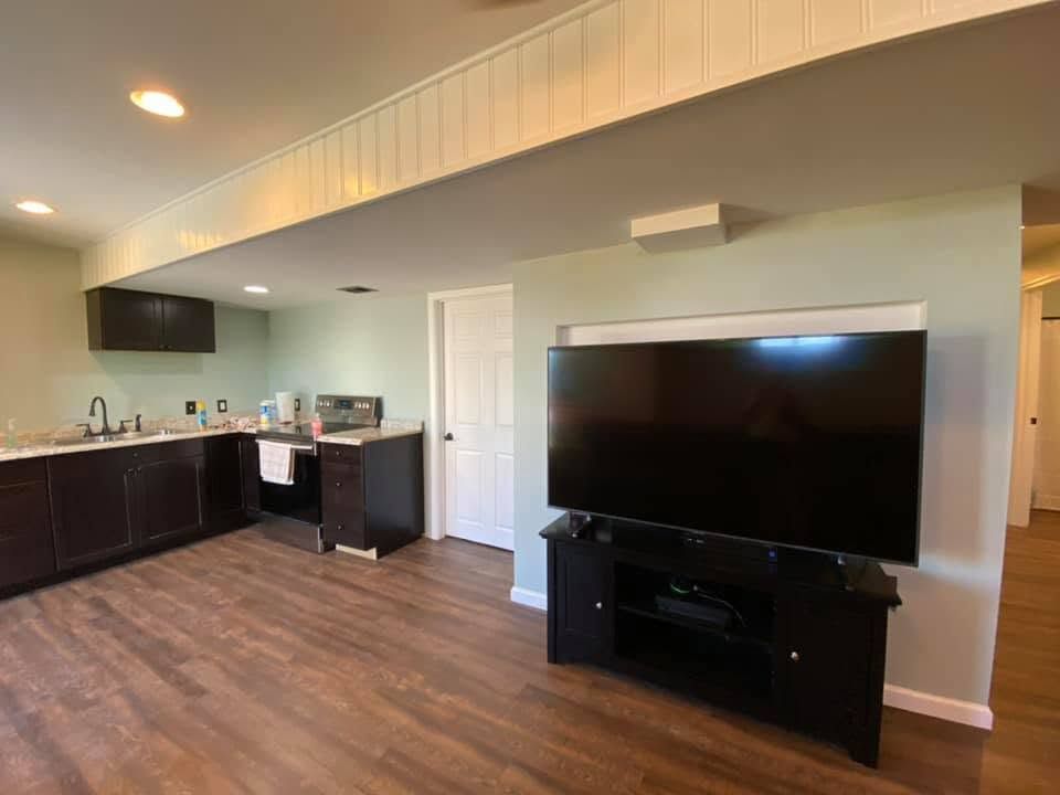 Empty modern living room with wood flooring, dark TV stand, and adjoining kitchen area