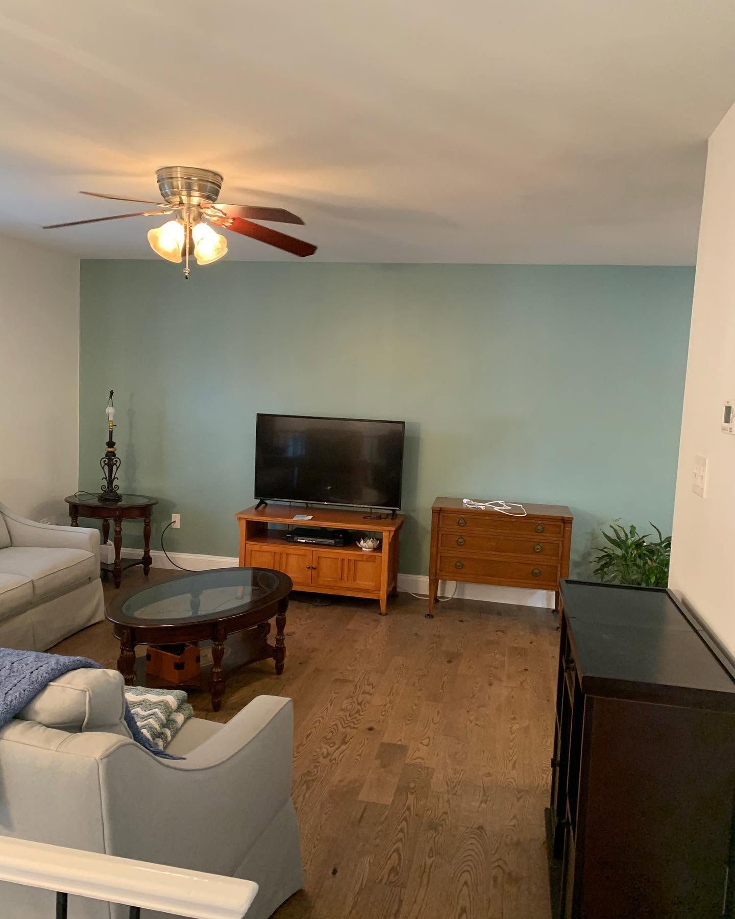 Living room with TV, ceiling fan, beige sofa, coffee table, and teal accent wall.