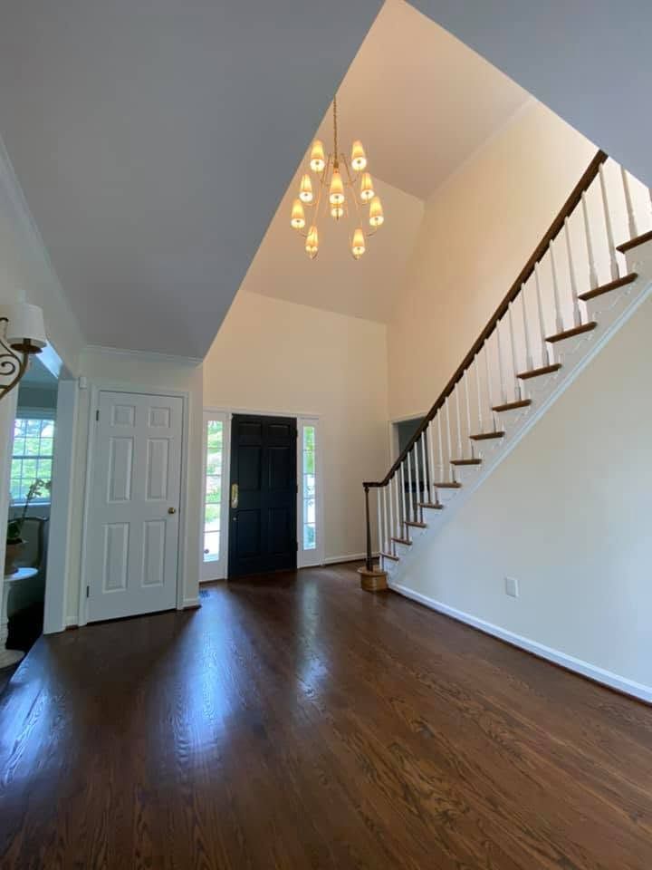 Empty foyer with hardwood floors, white staircase, open front door, and chandelier under a vaulted ceiling