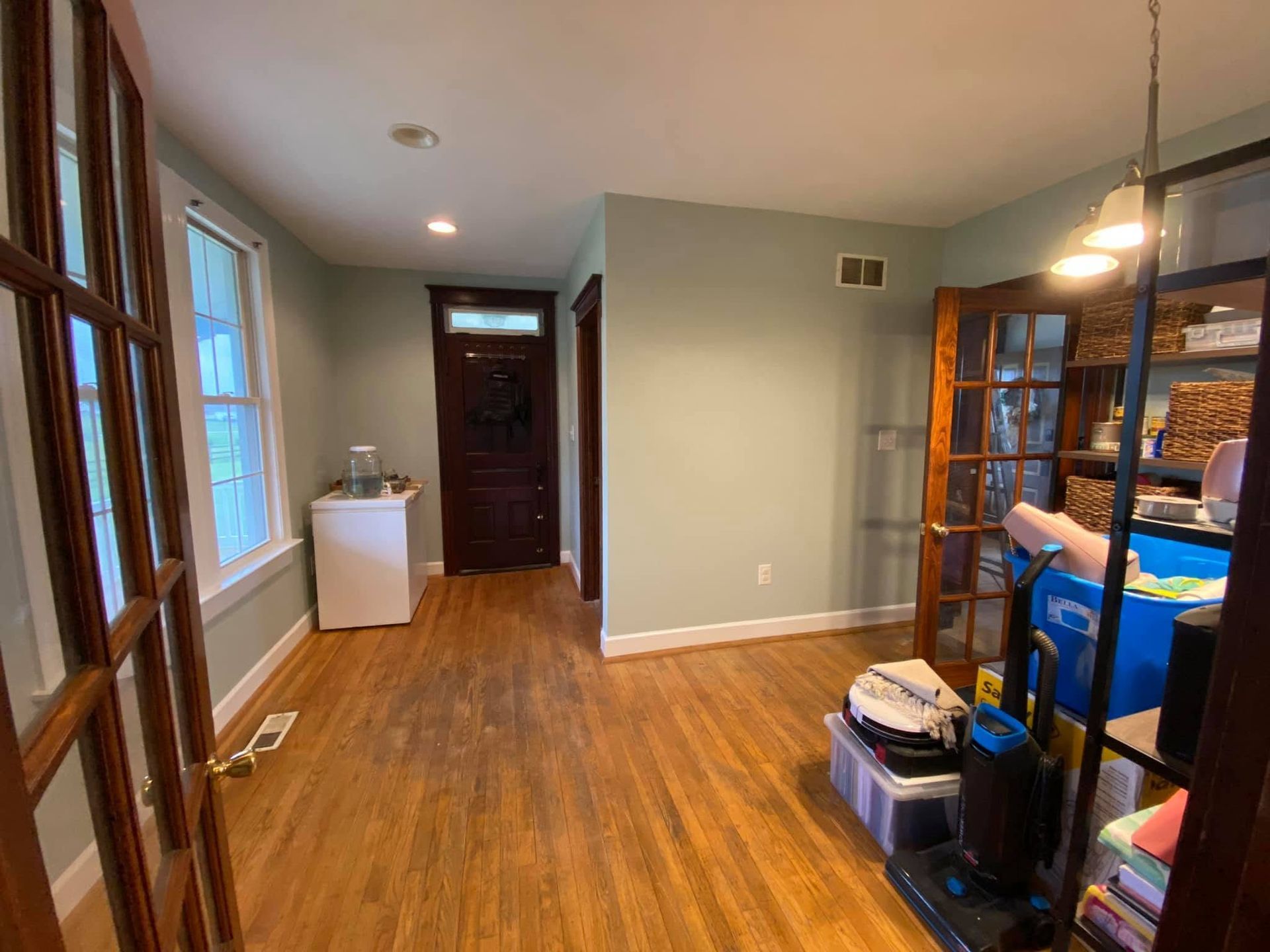 Empty hallway with wood floors, windows, a dark front door, and storage shelves on the right
