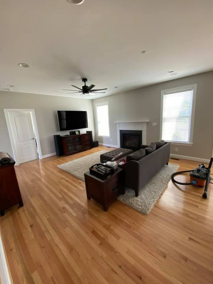 Bright living room with hardwood floors, gray sofa, TV, fireplace, and large windows