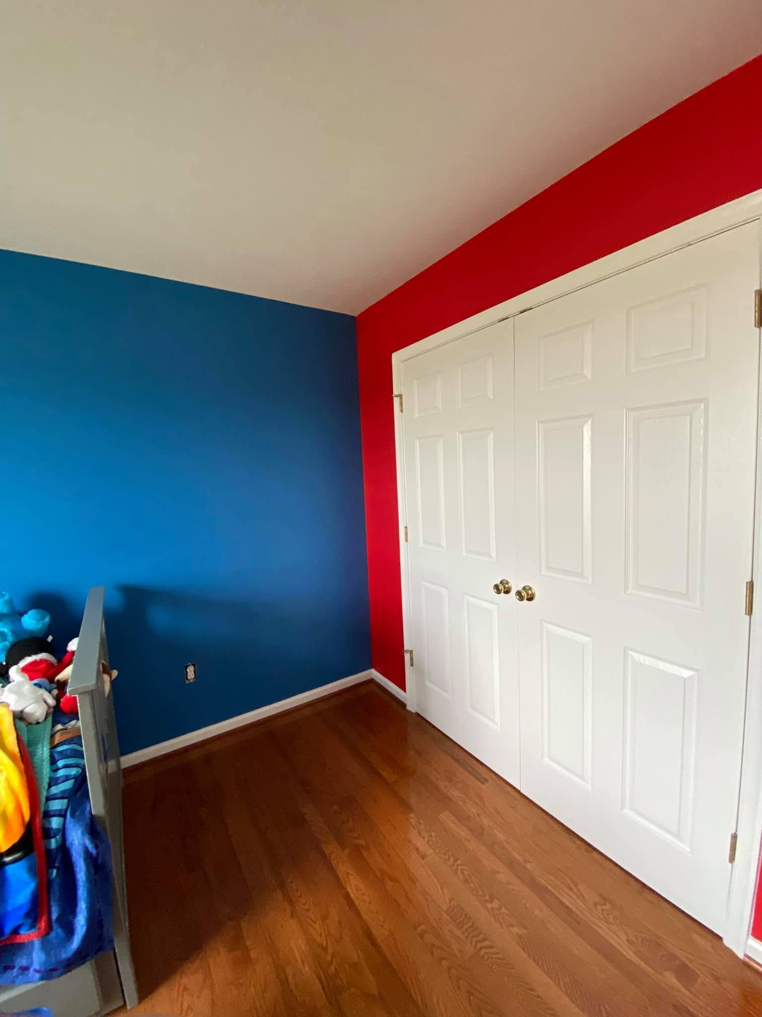 Empty bedroom with blue and red walls, white closet doors, and wood floor.