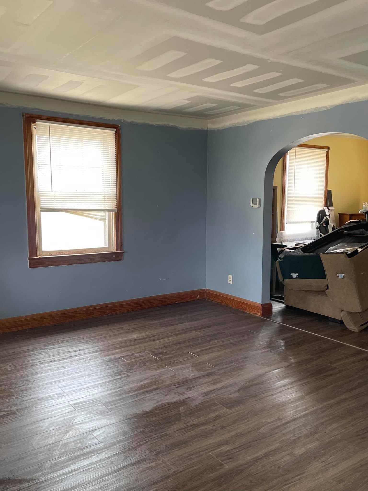 Empty room with blue walls, wood floor, patterned ceiling, and two windows.