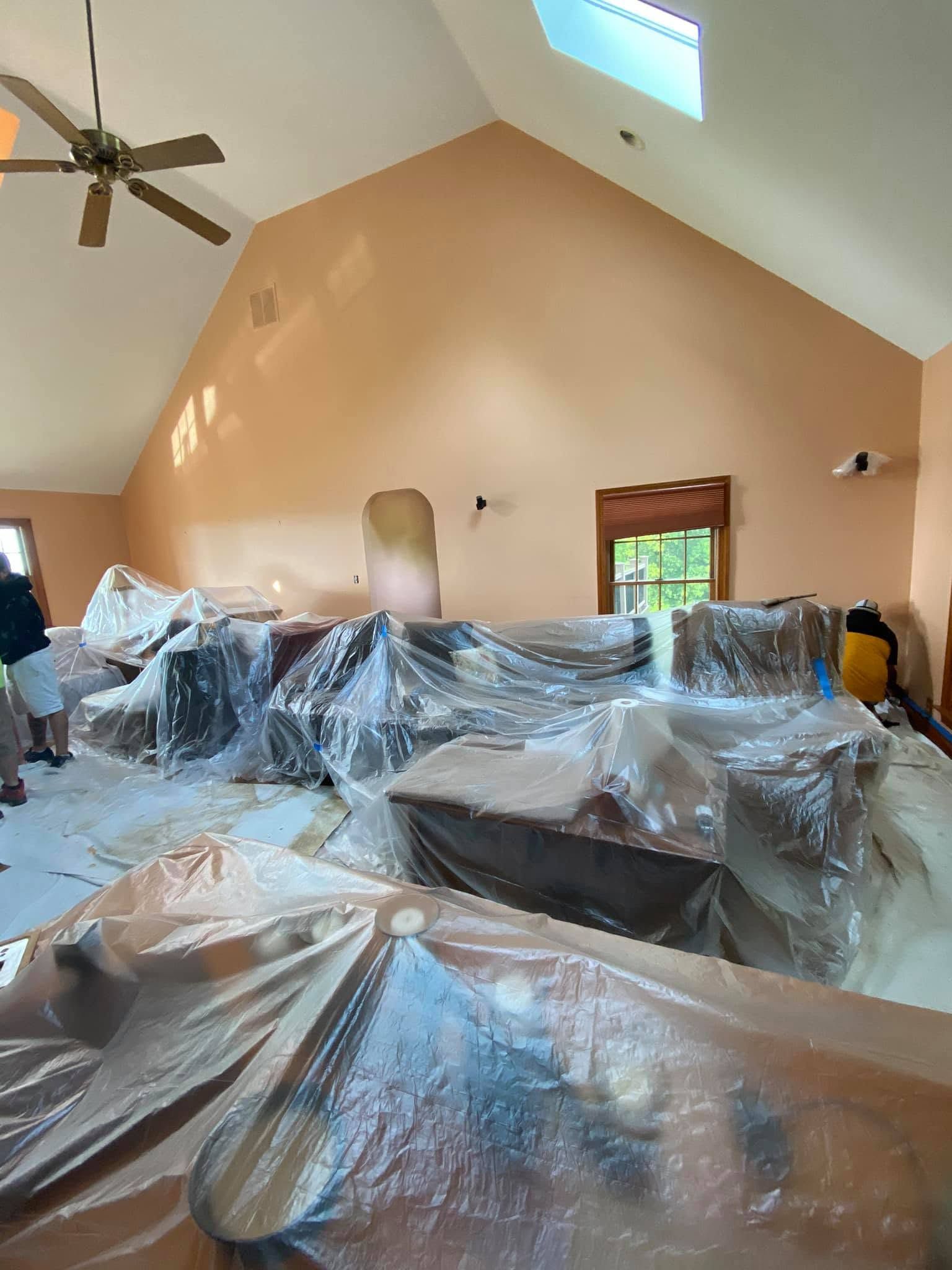 Living room with furniture wrapped in plastic, tan walls, ceiling fan, and skylight window