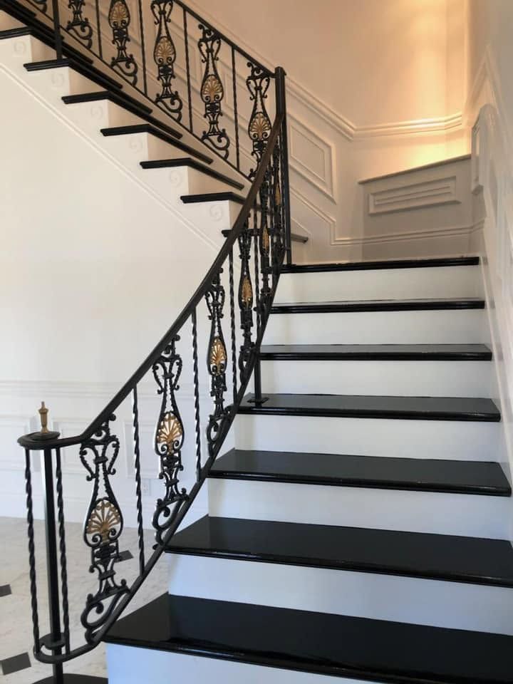 Elegant black wrought-iron staircase with white steps and decorative railing in a bright interior.