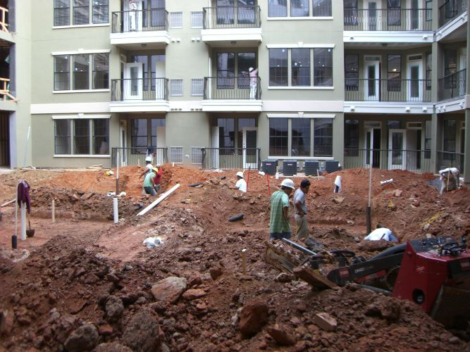 a group of construction workers are working in a dirt area in front of a building .