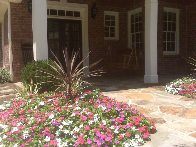 a brick house with a porch and flowers in front of it.