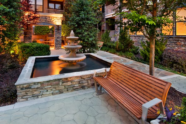 a wooden bench is sitting next to a fountain in a garden .