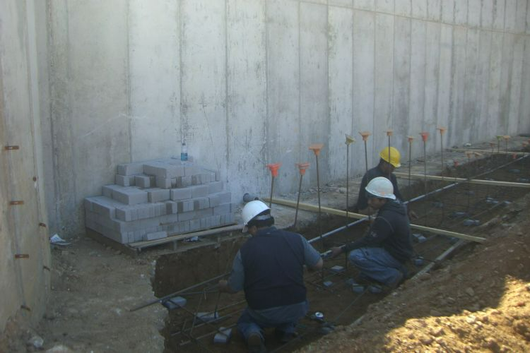 two construction workers are kneeling in the dirt in front of a concrete wall .