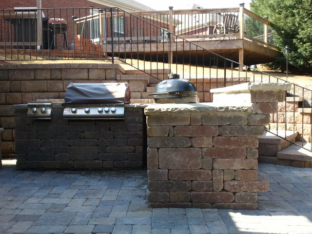 a brick patio with a grill and stairs leading to a deck
