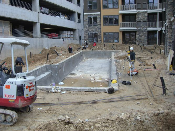 a swimming pool is being built in the dirt in front of a building .